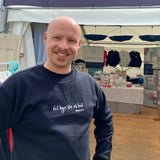 Elidyr Glyn wearing a black sweatshirt with the song lyrics Fel Hyn 'Da Ni Fod by Bwncath embroidered on the front