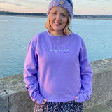 A digital lavender colour sweatshirt with the song lyrics Fel Hyn 'Da Ni Fod by Bwncath embroidered on the front